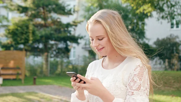 Молодая блондинка ходит и пользуется телефоном в городе — стоковое фото