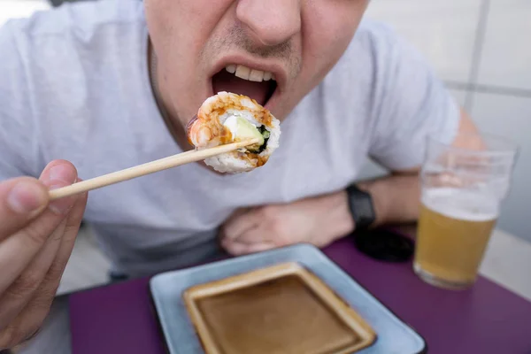 Sushi y boca chico primer plano. El tipo come sushi y rollos con palillos — Foto de Stock