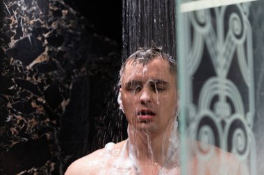 Adam duşta yıkanıyor. Karanlık duvarlarile Duş