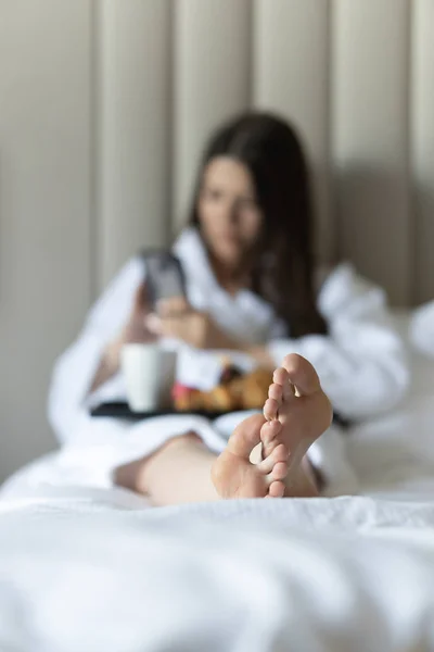 Женские ноги в постели. На заднем плане девушка с завтраком в постели — стоковое фото