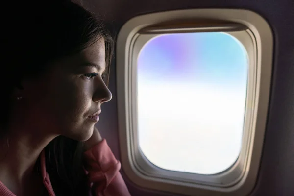Νεαρή γυναίκα ψάχνει μέσα από το παράθυρο σε αεροπλάνο Royalty Free Εικόνες Αρχείου