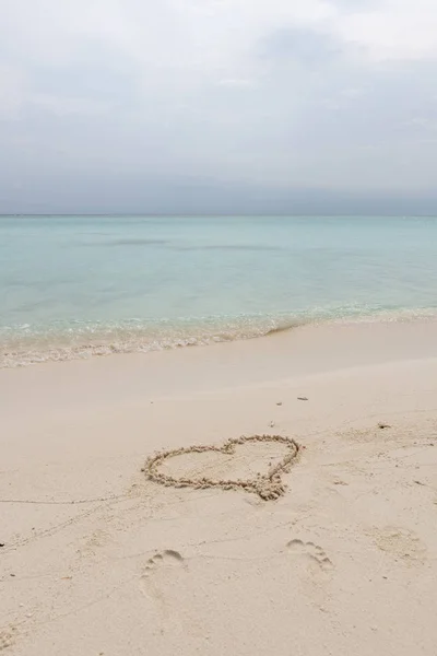 Tulisan tangan berbentuk hati di pantai oleh laut dengan gelombang putih dan latar belakang langit biru Stok Foto Bebas Royalti