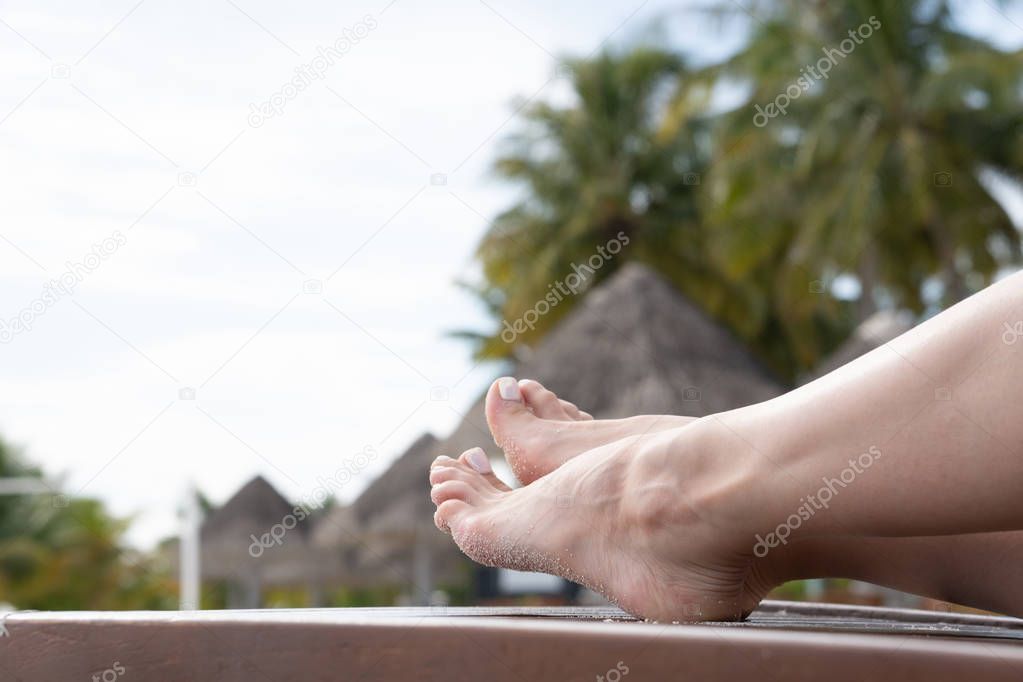 Female legs sunbathe on a lounger. Deckchair color dark wood.