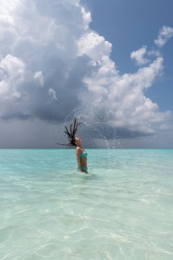 Genç bir kız saçlarını büyük ölçüde sudan çıkardığında su sıçratıyor..