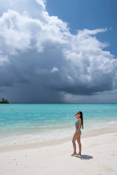 Een jong meisje in een turquoise zwempak staat op een wit strand. — Stockfoto