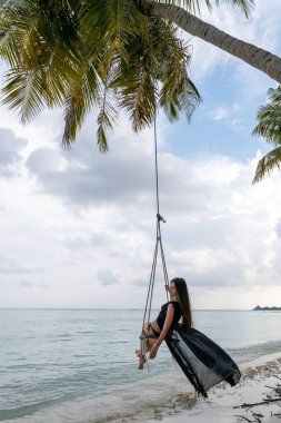 Esmer bir cennet adanın kıyısında bir salıncak üzerinde salıncak.