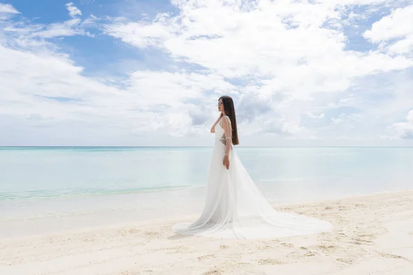 Den perfekta bruden. En ung brud i en vit klänning står på en Snövit strand. Stockbild