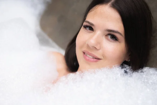 Een echte ontspannen voor een modern meisje. Mooie brunette neemt een bad met schuim. — Stockfoto