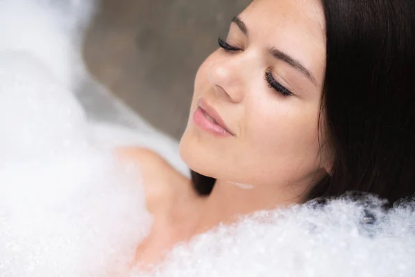 Een echte ontspannen voor een modern meisje. Mooie brunette neemt een bad met schuim. — Stockfoto