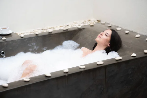 A real relax for a modern girl. Beautiful brunette takes a bath with foam. — Stock Photo, Image