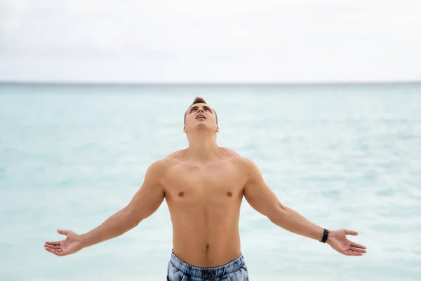 Сильный молодой парень с голой грудью смотрит в рай. На заднем плане океан Лицензионные Стоковые Фото