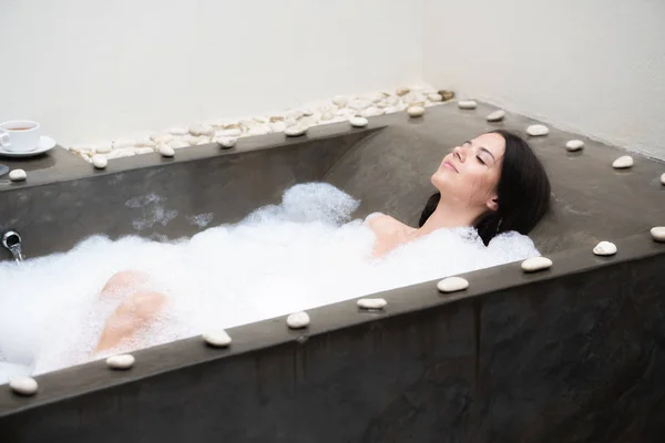 En riktig Relax för en modern tjej. Vacker brunett tar ett bad med skum. Royaltyfria Stockfoton