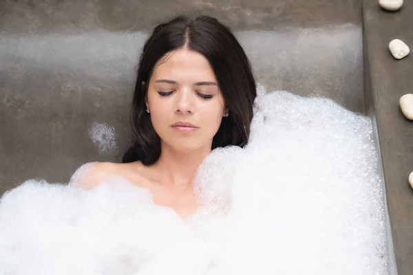 Um verdadeiro relaxamento para uma garota moderna. Linda morena toma um banho com espuma . — Fotografia de Stock