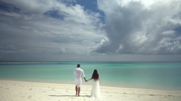 Nygifta hålla händerna på en vacker vit sandstrand och turkos vatten. — Stockvideo