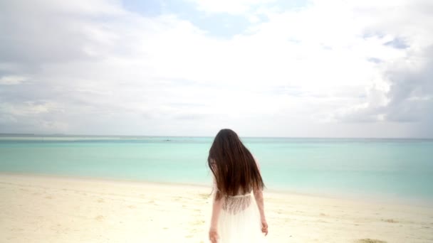 Una joven novia con un vestido blanco está bailando en una playa blanca como la nieve . — Vídeos de Stock