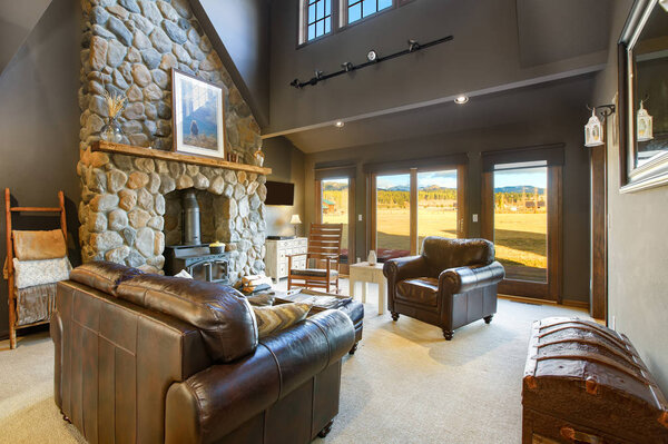 Amazing grey living room boasts river rock fireplace, leather furniture and mountain view from the window.