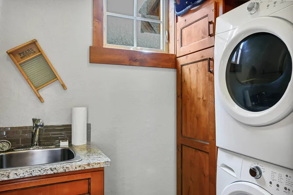 洗衣房 配有堆叠式洗衣机和烘干机 旁边有深色木柜和水槽 — 图库照片
