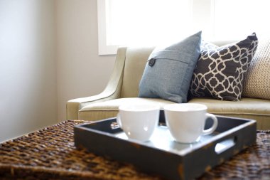 Rattan gövde sehpa ahşap tepsi ve bej kanepe renkli yastıklar ile yanındaki beyaz kupa ile yakın çekim