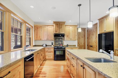 Hafif ahşap dolaplar, granit tezgahlar ve siyah aletleri ile güzel mutfak.