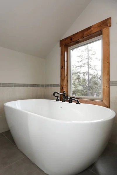 ビュー ウィンドウの下で独立した浴槽をなめらかなオイルと対になって白い浴室の設計の青銅製の蛇口をこすり — ストック写真