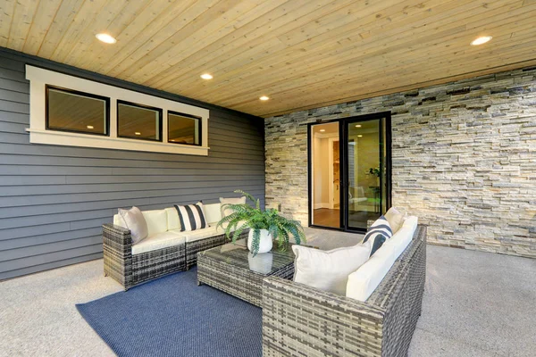 Luxury modern house exterior with covered patio boasting stone fireplace and cozy rattan furniture