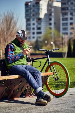 Bir bisiklet ve bir akıllı telefon olan genç bir adam şehirde bir bankta dinleniyor. Güneşli gün