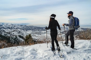 Travelers in the mountains walk on snowshoes. The guy with the girl on the edge of the hill look into the distance. View from the back. Winter mountain tourism. Kazakhstan