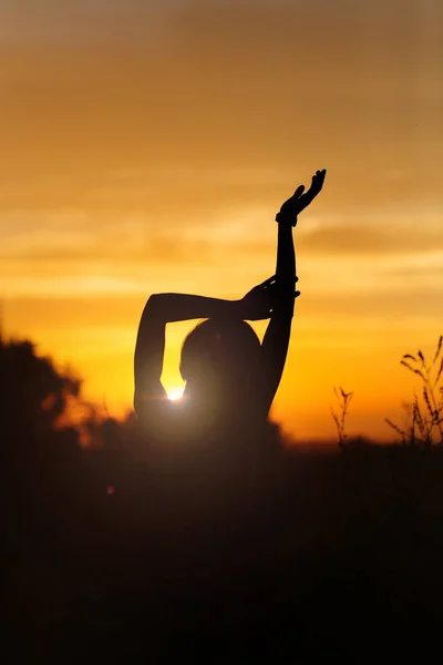 Silhouette of a girl with raised hands against the backdrop of the sunset outdoors — Stock Photo, Image
