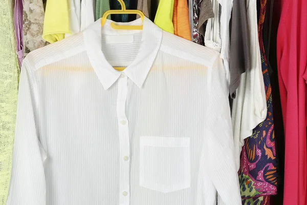 white transparent blouse on hanger in front of other female clothes in the closet