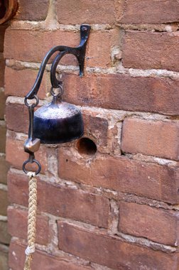 Bahçenin girişindeki tuğla duvarda ipi çeken çan.