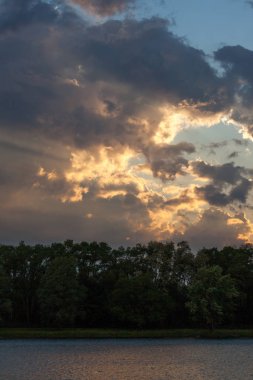 Işıktan fırtına bulutları üzerinde batan güneşin muhteşem bir görüntü gölge bahar ağaçları bir satırın üstüne mavi gökyüzünde bir açılış ile.