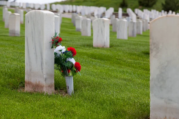 丘の中腹に活気に満ちた春の草との軍事墓地大理石の墓石に寄りかかって赤白と青の花のグループ — ストック写真