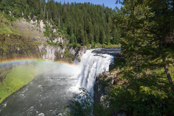 A rainbow in the mist of Upper Mesa Falls as it cascades over a cliff in the rugged wilderness of Henrys Fork of the Snake River along the Mesa Falls Scenic Byway in Idaho.