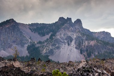 Paulina Peak standing tall in a stormy sky with rock slides down the side and a great lava obsidian flow at the base in Newberry National Volcanic Monument in Central Oregon. clipart