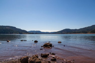 Lost Creek Gölü 'nün yüzeyinden William L. Jess Barajı' na kayalık bir ön planda ve uzaktaki Cascade Dağları 'na bakıyoruz..