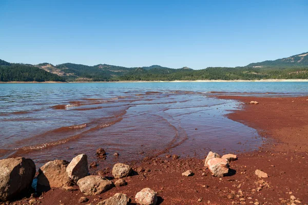 Low water levels reveal red clay and rocks at Lost Creak Lake near Prospect, Oregon located in the Cascade Mountain Range.
