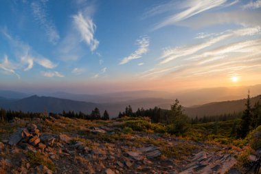 Yakındaki bir yangından çıkan duman tabakaları Prospect, Oregon yakınlarındaki Kırmızı Battaniye Dağı 'nın tepesinden görülen Cascade Dağları' nın üzerindeki batan güneşe turuncu bir parıltı verir..
