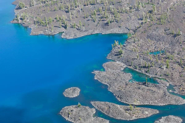 ウィザード島の西端を見下ろすと 火口湖国立公園の青とターコイズブルーの水に大きな常緑樹が散りばめられた火山岩の表面 — ストック写真