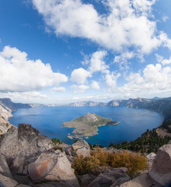 A dramatic high elevation view of the deep blue Crater Lake and Wizard Island from Watchman Tower on the Western rim with white fluffy clouds in late summer. clipart