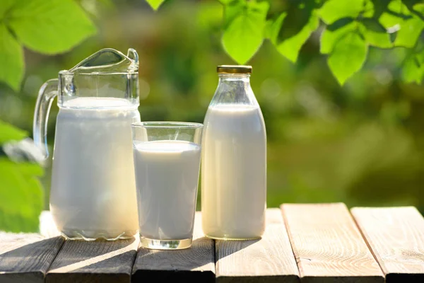 Glas und Krug mit frischer Milch auf Holztisch — Stockfoto