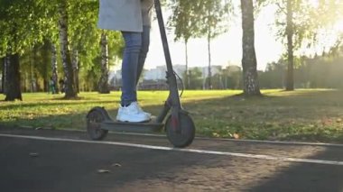 Kız şehir parkında e-scooter kullanıyor.