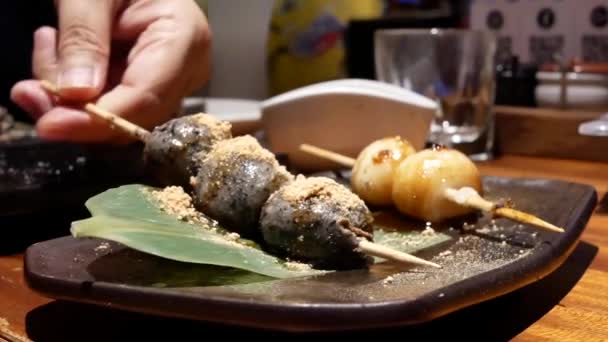吃日式烤团子烧烤和芝麻酱的人的运动在餐桌内的日本餐厅 — 图库视频影像