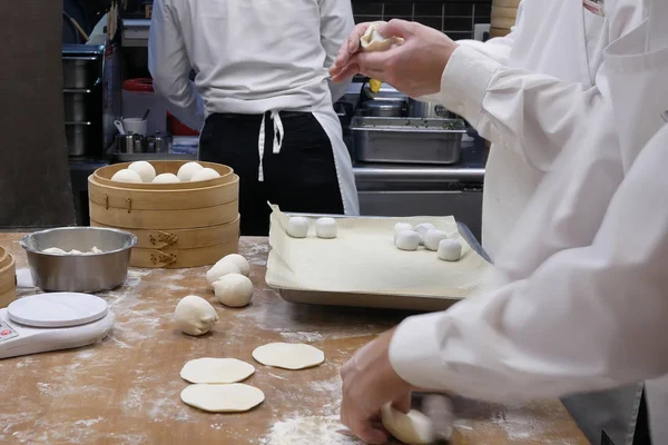 人们的动作是在餐馆厨房里把面团做饺子之前揉面团的运动 — 图库照片