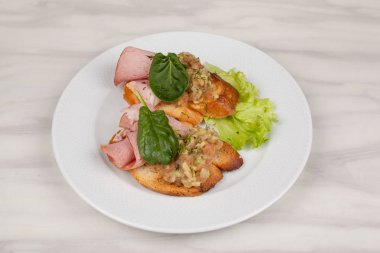 Jambon ve otlar beyaz tabakta sandviç.