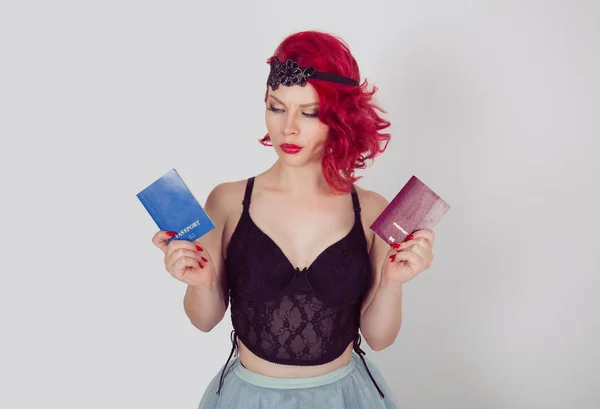 I don\'t like my non-European citizenship concept. Portrait young woman holding two passports one European burgundy red and looking doubtful to the blue non-EU confused face expression on white gray
