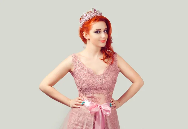 Confident beauty pageant queen. Serious woman in purple pink pearls crown in nude color pink lace dress vogue style with red head curly wavy hair curls looking at you camera on light green background