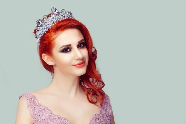 Confident sexy beauty pageant queen. Smiling slightly redhead woman in crown with purple pearls crystals, violet pink color lace dress vogue style curly wavy hair curls looking at you green background