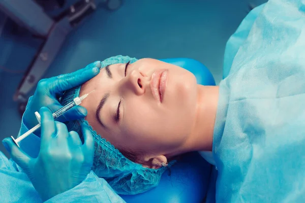 İçerik çekici model gözleri kapalı bir klinik cerrahi oda; alnından botulinum toksin hyaluronik asit enjeksiyonu sahip Ameliyathane arka plan. Yüz kavramı için filler güzelleştirmek