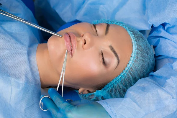 Güzellik uzmanı el dudak cerrahisi araçları kadın ağız yakın tutarak sonuçları kontrol sonra kapatın. Elinde cımbız ve makas var. Güzel kadın yordamı ile zevk alıyor