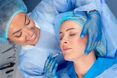 Doktor bir kozmetik enjeksiyon hasta gözlerle uzanmış bir ameliyat odası, ameliyathane dudak kapalı olgun orta yaş alt dudak dolgu yapar, kavram güzelleştirmek.